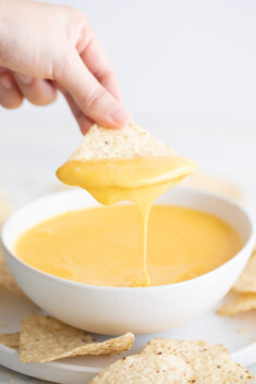 一只手蘸着玉米饼片蘸着一碗素食奶酪的照片