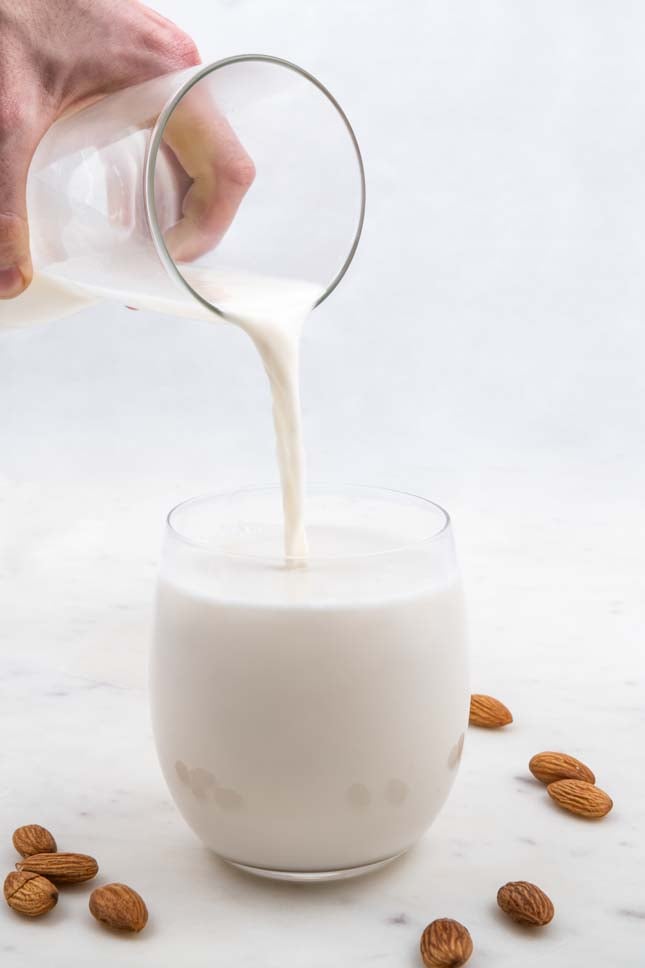 一个罐子把自制的杏仁牛奶倒进玻璃杯的照片